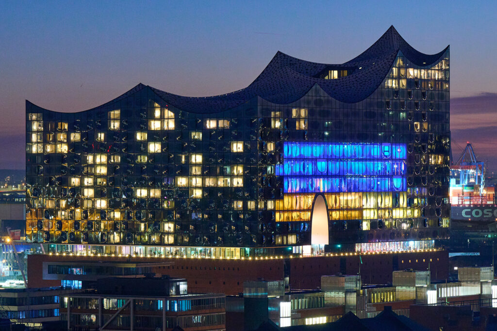 Unsere Fotografin Catrin-Anja Eichinger nahm das blau-gelbe Elbphilharmonie-Solidaritäts-Foto mit einer Nikon Z6II und einem Nikkor-Z-Objektiv mit Brennweite 135 mm, Blende 7,1 am 26.02.22 um 18:52 auf – vom Kirchturm St. Katharinen. © Catrin-Anja Eichinger