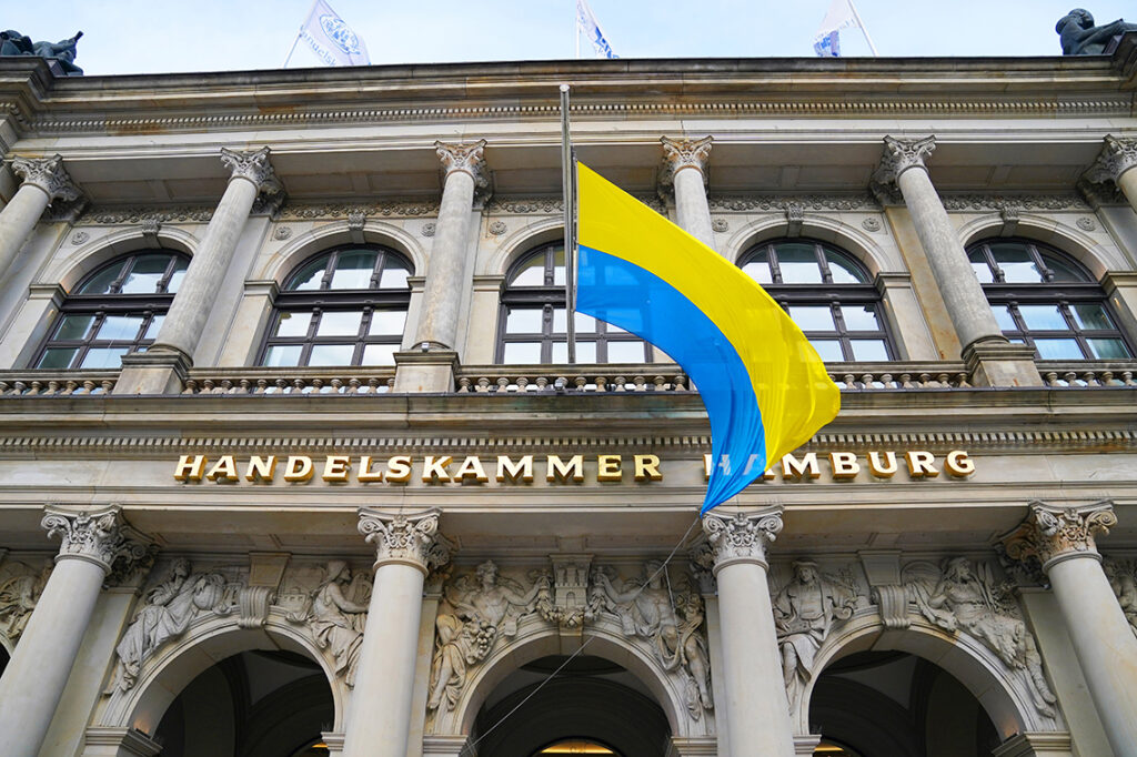 Aus Solidarität weht die Flagge der Ukraine seit Donnerstag, 24. Februar 2022, dem Überfall Russlands auf die Ukraine, über dem Eingang der Handelskammer Hamburg. © picture alliance/dpa | Marcus Brandt