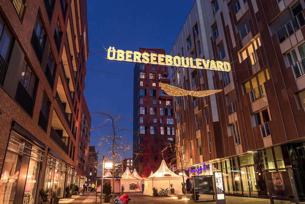 Festlich leuchtet der Überseeboulevard in der Vorweihnachtszeit mit seinen Schaufenstern, den weißen festlichen Zelten und – natürlich – mit dem großen Weihnachtsbaum im Zentrum der Flaniermeile im nördlichen Überseequartier – für alle Anwohner:innen und Klönschnacker:innen aus der HafenCity und gerne auch ganz Hamburg. © Florian Janssen